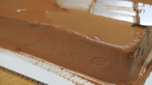 slow motion baker smoothing edge of chocolate cake slow motion. Baker uses metal spatula to form and smooth chocolate icing on a rectangle single layer chocolate cake.