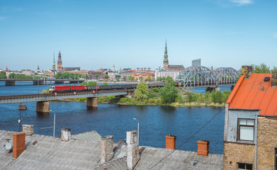 Fototapeta premium Panoramic view of Riga city covered in clouds. Iconic railroad bridge and old town panorama across the river Daugava. Picturesque scenery of historical architecture. National library of Latvia.