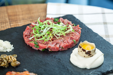 Close up view on fresh steak beef tartare served on dark stone plate with sauce and raw quail egg. Selective focus. Copy space for design. Picture for menu