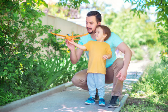 Dad and toddler son together launch toy airplane, both man and boy are looking cheerfully at plane. Father and son spending good time together, family relationships concept