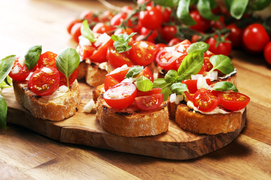 Traditional italian antipasto bruschetta appetizer with cherry tomatoes, cream cheese, basil leaves and balsamic vinegar on cutting board. Antipasti