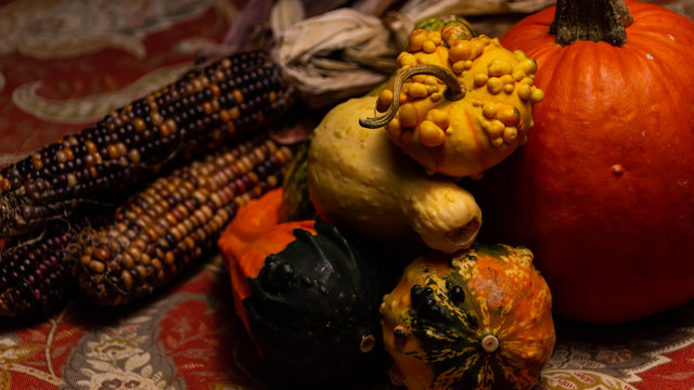 Colorful corn, pumpkins, squash, and gourds lie on a table.