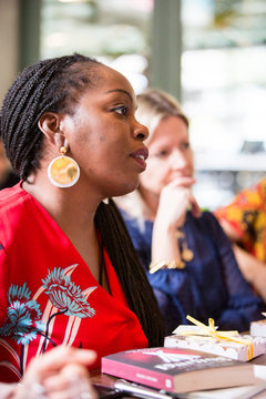 Woman with cornrows wearing golden earrings and red top sitting at  a table, listening attentively.,Oxfordshire