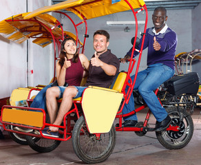 Fototapeta na wymiar Happy young couple sitting on rickshaw with friendly African American driver, ready for tour of city