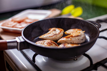 Closeup of chicken meat strips cooking on a hot pan on a gas stove