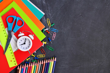 Bright stationery on a black Board background notebooks, pencils, scissors and others.