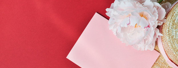 The envelope and pink peony flower next to the straw hat on a red background.