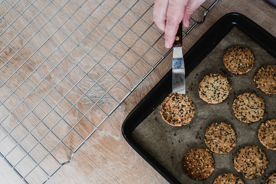 High angle close up of person removing freshly baked seeded crackers from a baking tray.