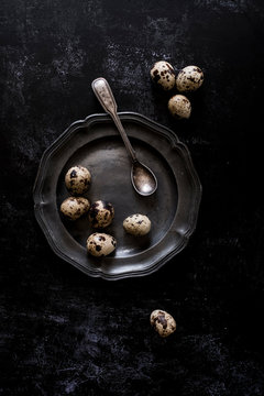 A pewter plate with small spotted quail's eggs and a spoon.