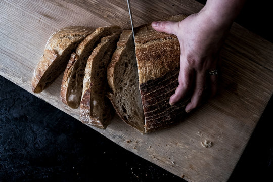 A hand holding a loaf of bread and using a breadknife to cut slces.