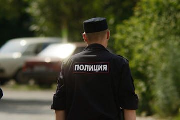Obraz premium Russian policeman patrols street of provincial town. Man in police uniform go in direction of russian cars. Inscription 