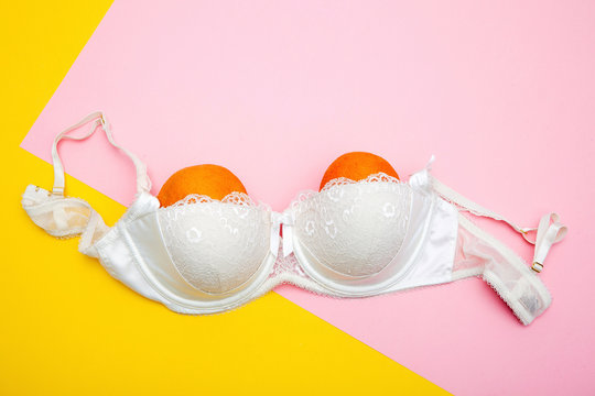 view of white bra with two oranges on pink and yellow, breasts concept