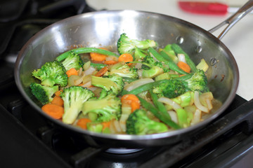 Stir fry vegetables cooking in a stainless steel pan on a natural gas stove.