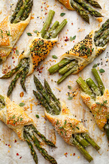 Baked green asparagus in puff pastry sprinkled with sesame seeds, nigella seeds and fresh thyme on a white background, close-up, top view. Puff pastry bundles