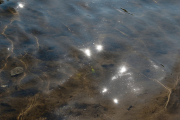At the bottom of the river is visible relief. The stones cast a shadow, the waves cast solar glare to the bottom. Solar reflections in the form of lanterns shine from above on the water.