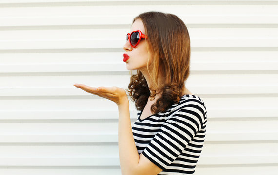 Portrait close-up young woman blowing red lips sending sweet air kiss on white wall background