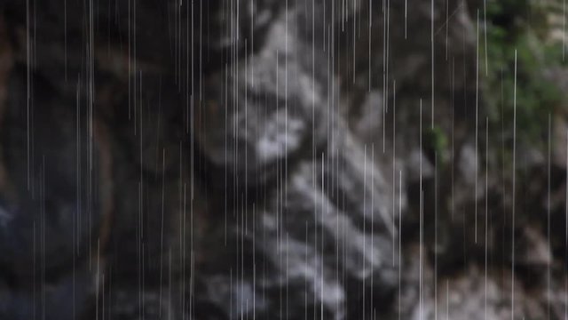 Punto de enfoque en Gotas de agua formando una lluvia en rayas  sobre fondo de rocas borrosas. Imagen real 