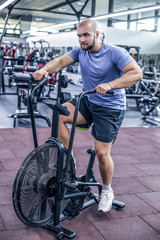 young man using exercise bike at the gym. Fitness male using air bike for cardio workout at crossfit gym.