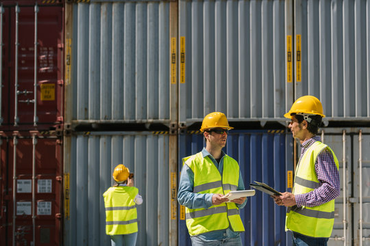 Workers talking near stack of cargo containers on industrial site