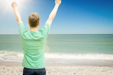 Mann streckt am Meer die Arme in den Himmel