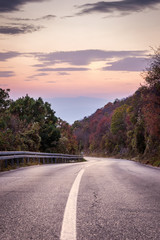 Curvy mountain road with white line, autumn colors and beautiful sunset sky and sunlit rocks