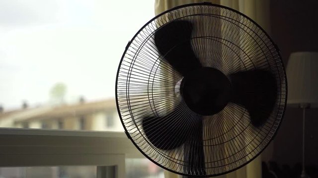 Using remote to turn on articulating fan in living room near a window.