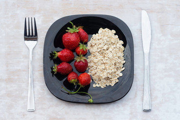 Black plate with oatmeal and strawberries on white background. Healthy breakfast. The concept of healthy eating.