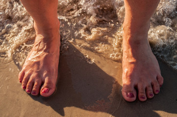 Women's feet are on the sand. On the nails, the applied nail Polish.