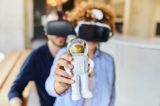 Man and woman wearing VR glasses holding astronaut figurine