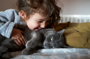 Close up of smiling girl cuddling gray cat on bed at home