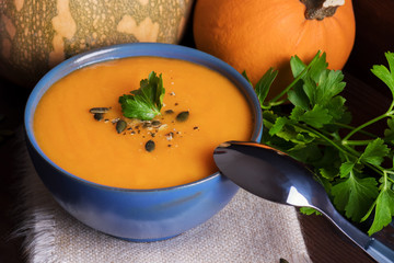 Pumpkin soup in a bowl served with parsley, olive oil and pumpkin seeds. Vegan soup. Dark wooden background.