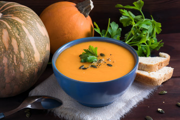 Pumpkin soup in a bowl served with parsley, olive oil and pumpkin seeds. Vegan soup. Dark wooden background.