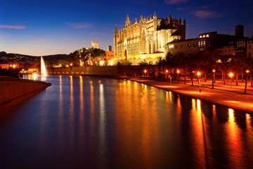 Fototapeta premium Palma cathedral illuminated at dusk with lake, fountain and reflections on water, mallorca, spain.