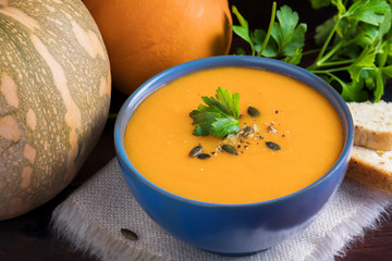 Pumpkin soup in a bowl served with parsley, olive oil and pumpkin seeds. Vegan soup. Dark wooden background.