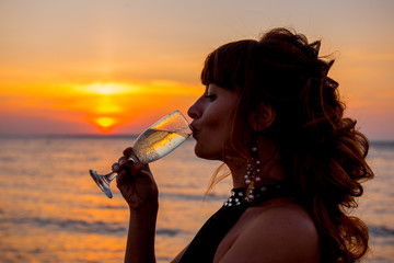 woman at sunset. Champagne on the beach. Elegant girl is drinking champagne on romantic date in the evening. Vacation alone. girl drinking wine at sunset near the ocean
