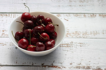 Cherries in a white deep plate on a white wooden background and a place for the inscription.