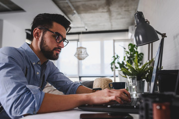 Young modern bearded man working with laptop computer indoors