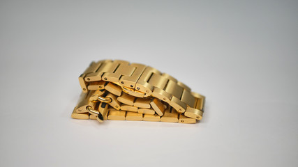 A shiny gold colored metal chain link wrist watch band laying folded on a white table.