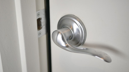 A white door ajar with brushed nickel lever handle and a dark room beyond waiting to be entered.