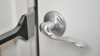 A white door ajar with brushed nickel lever handle.  A black pry bar is being used to force open...