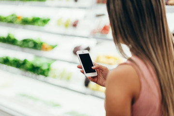 Woman using mobile phone while shopping in supermarket