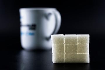 Sugar cubes were arranged in square shape. Background with white and patterned hearts. Black background.