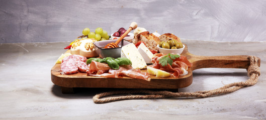 Cutting board with prosciutto, salami, cheese,bread and olives on dark stone background