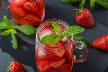 Fresh strawberry smoothie. Fresh summer cocktail with strawberries and ice cubes on a dark background on a black wooden table.
