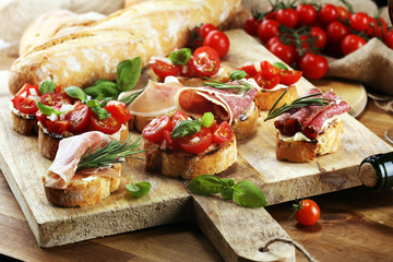 antipasto various appetizer. Cutting board with prosciutto, salami, cheese, bread and olives on dark wooden background