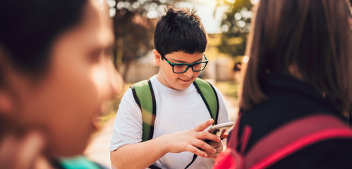 Boy standing with classmates using smart phone at schoolyard
