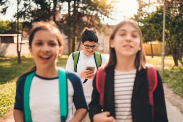 Boy walking with classmates using smart phone at schoolyard