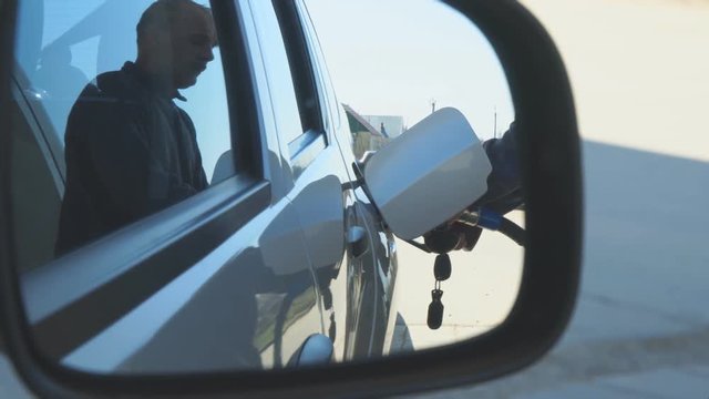A man refills a gasoline car. View through the rearview mirror