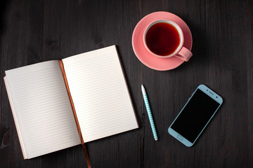 Obraz na płótnie Canvas Open book, cup of tea, pen, phone on a black background