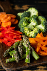 Assorted mix of raw vegetables - carrot, paper, asparagus, broccoli and greens on wooden table background.